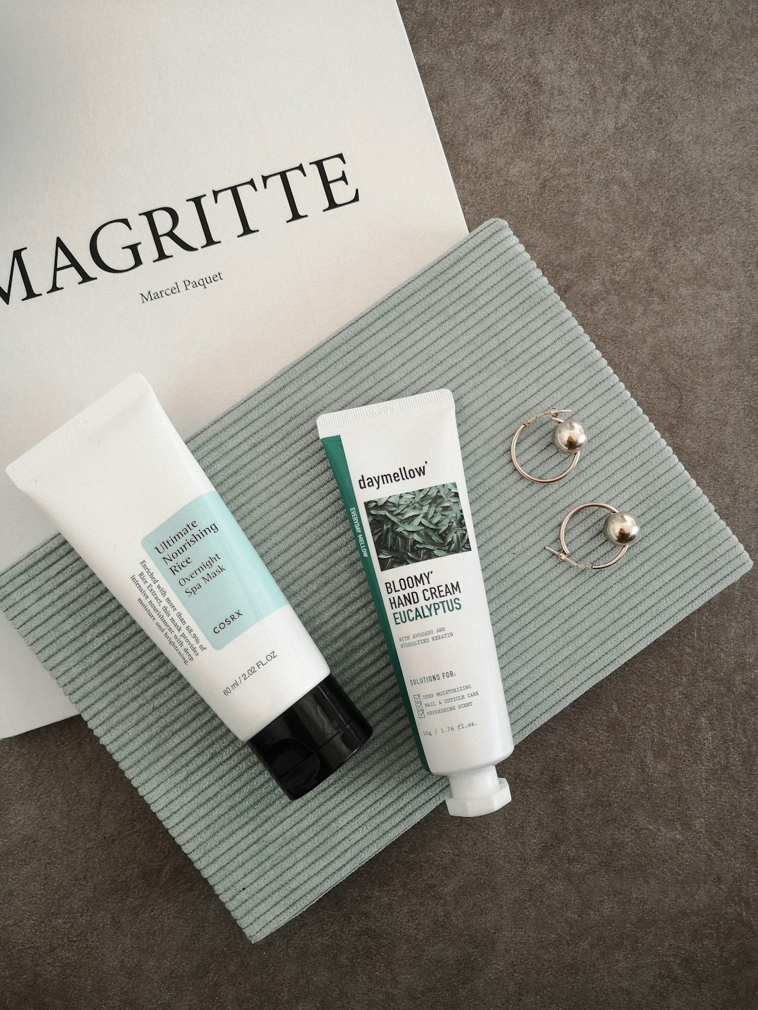 An overnight spa mask and oil serum in a flatlay with a green velvet notebook, a tote bag, and gold earrings.